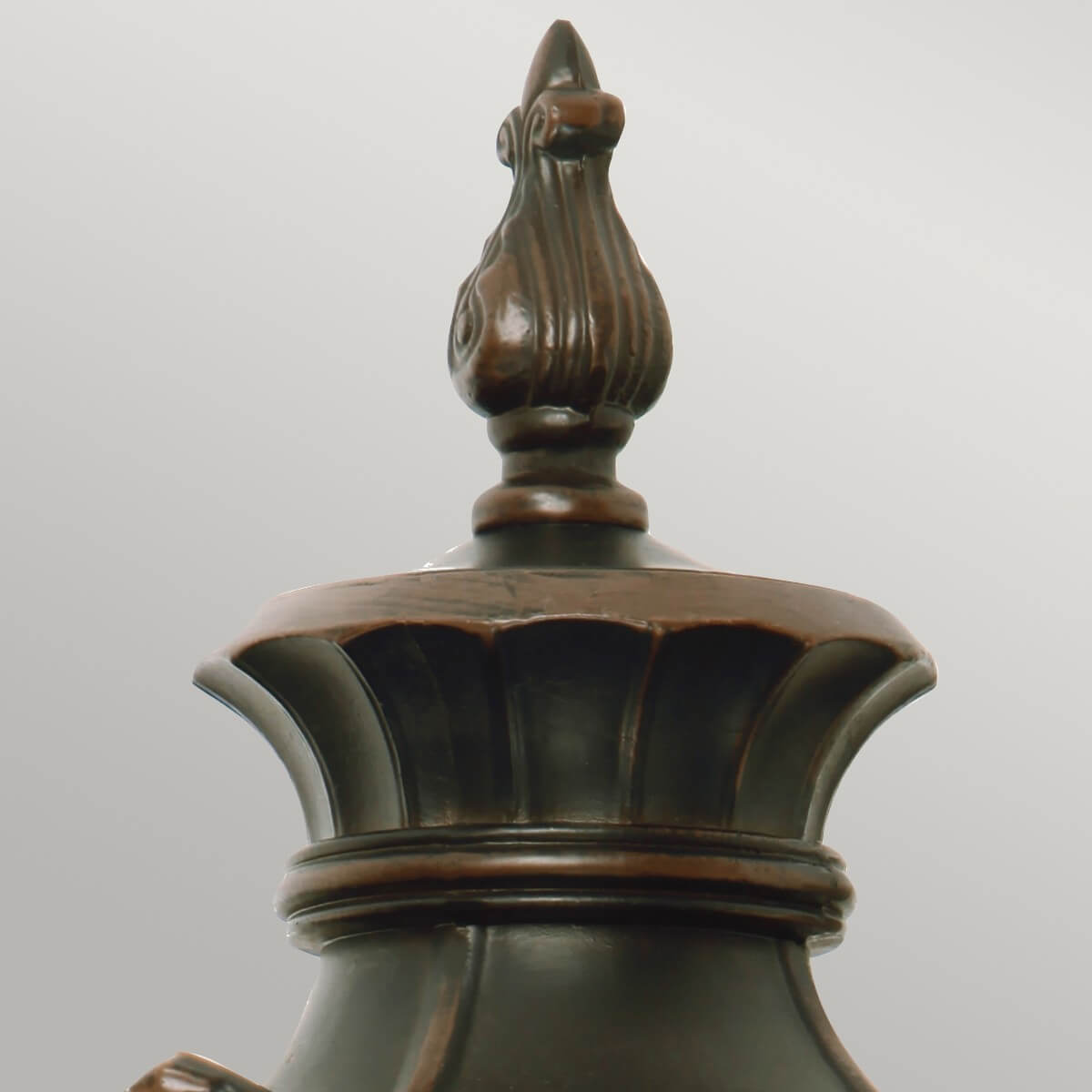 Détail du sommet mouluré avec pointe ornementale et finition bronze patiné.