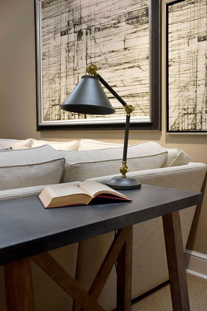 Lampe de bureau sur console devant canapé, livre ouvert et tableaux au mur
