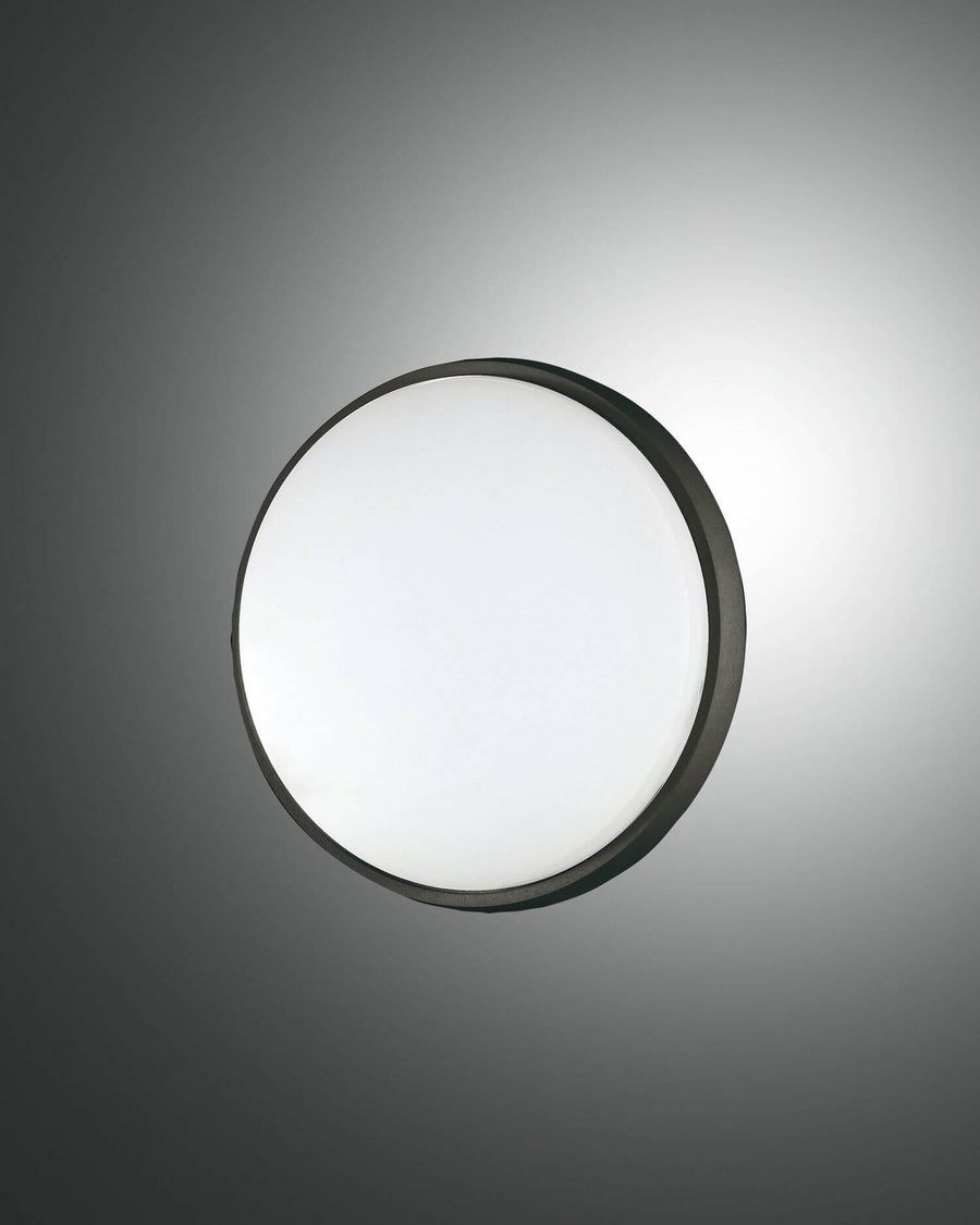 Plafonnier rond noir vu de face sur fond gris, verre opalin diffusant une lumière blanche