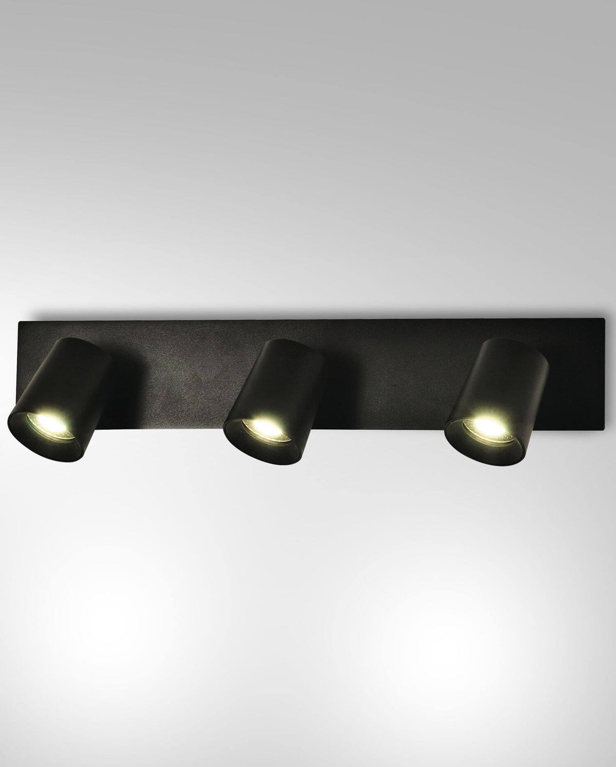 Luminaire mural noir trois spots cylindriques allumés, vue de face sur fond gris clair