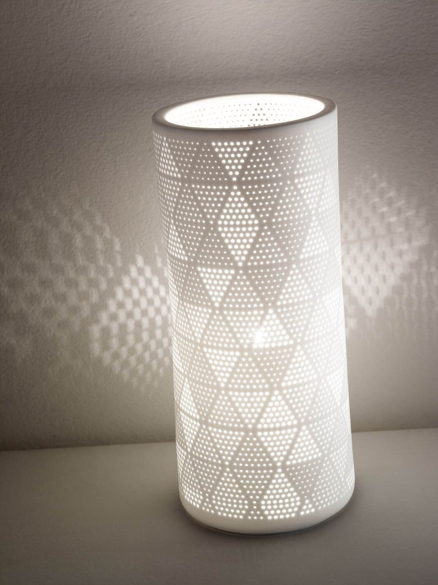 Lampe allumée contre un mur, ombres géométriques dessinées par les perforations