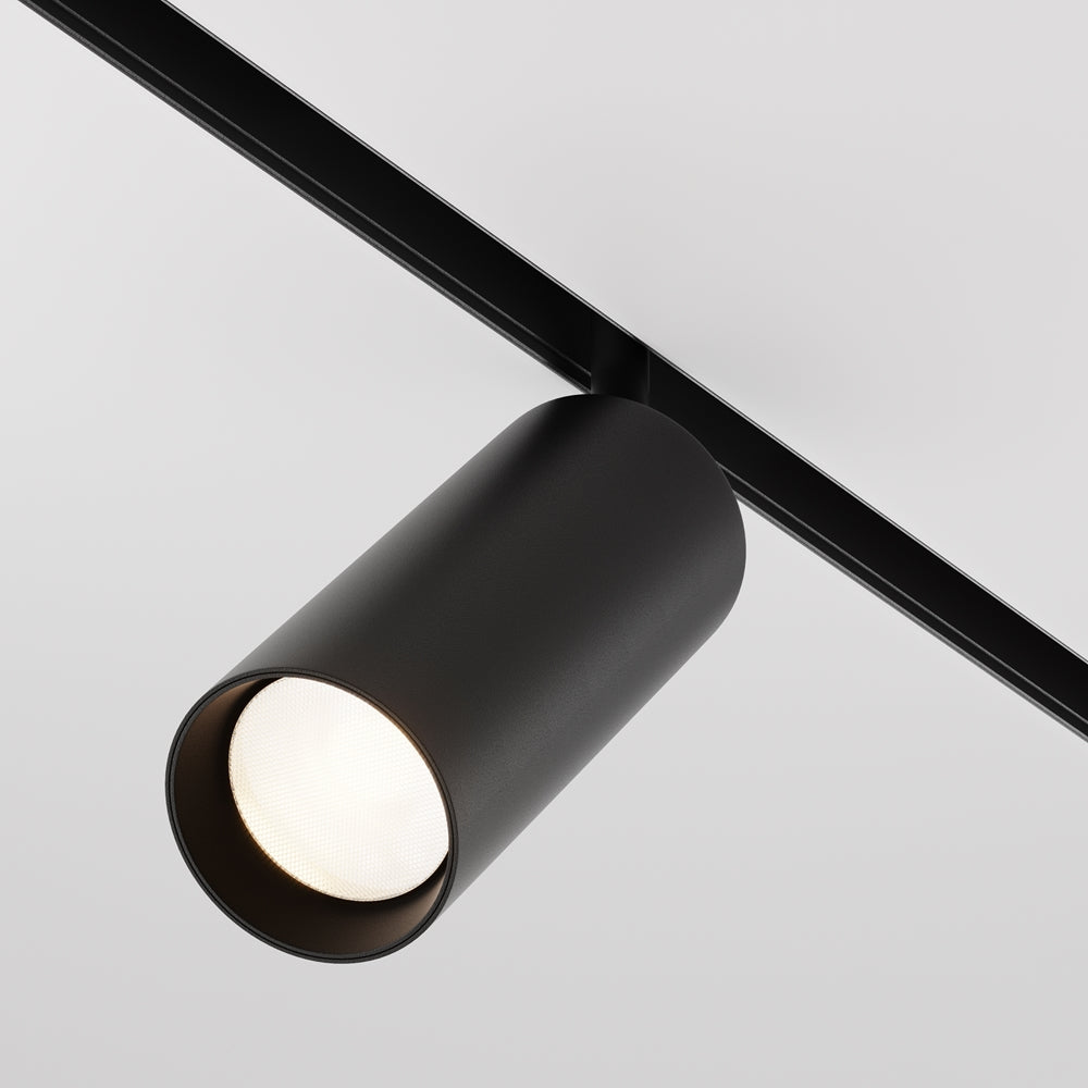 Projecteur cylindrique noir fixé sur rail, orienté vers le bas sur fond gris clair