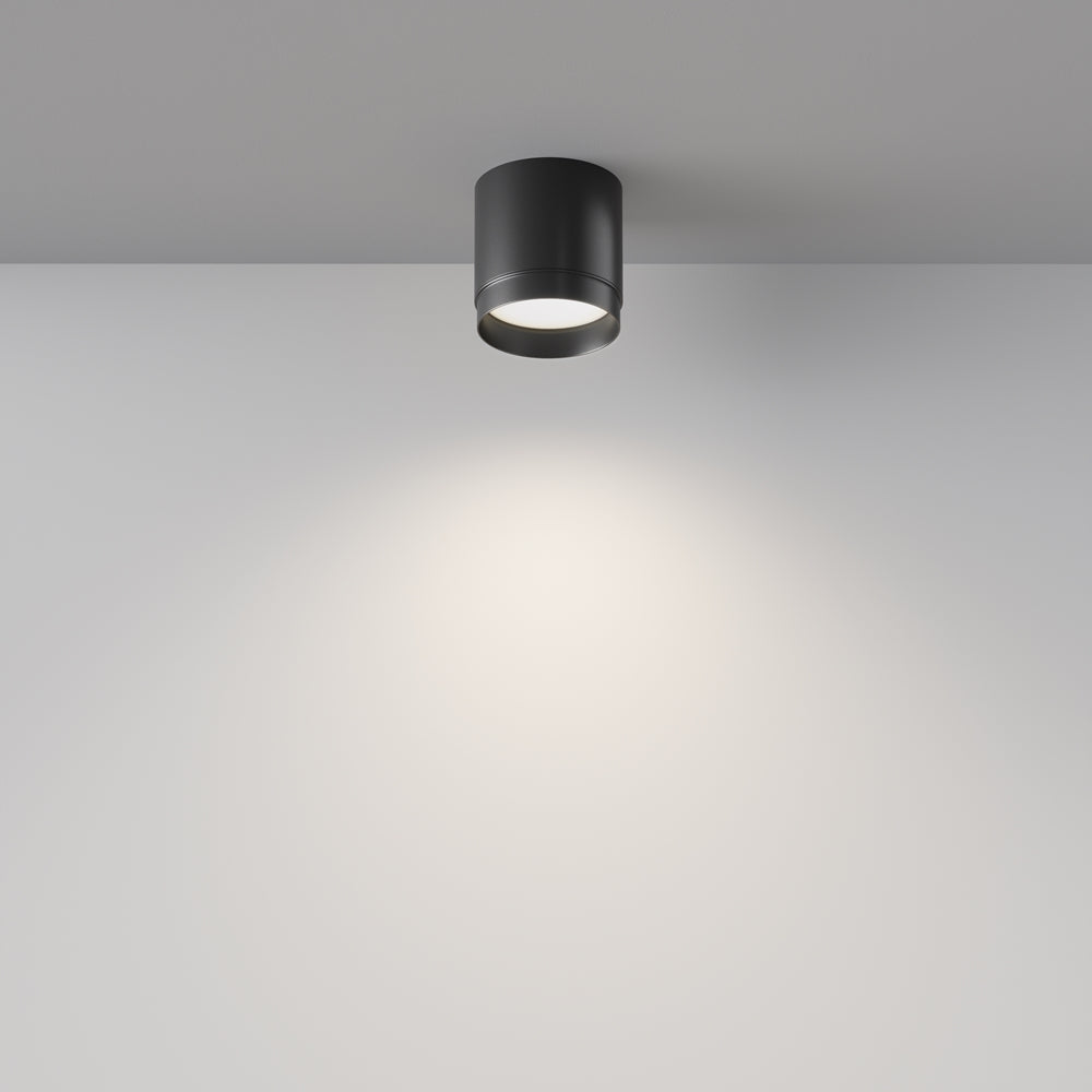 Plafonnier noir allumé au plafond, halo lumineux doux sur le mur