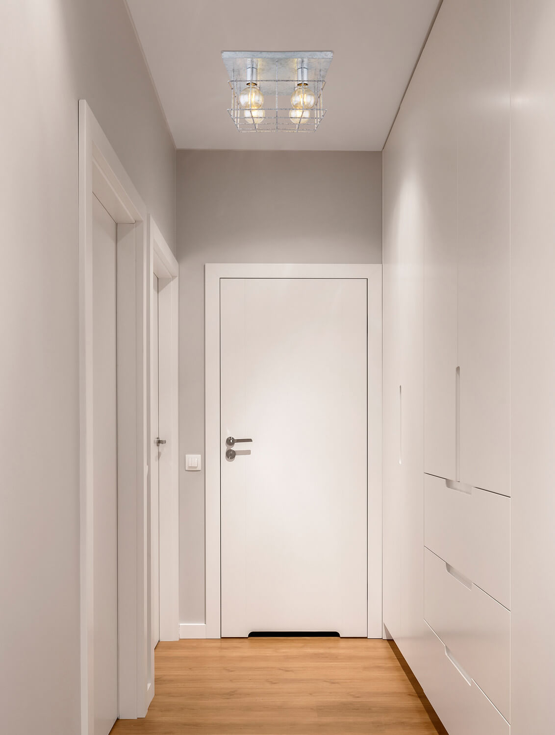 Mise en ambiance dans un couloir blanc, luminaire fixé au plafond au-dessus du sol en bois
