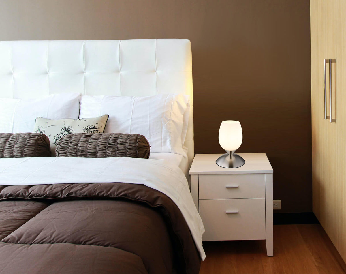 Mise en ambiance dans une chambre, lampe posée sur table de nuit près du lit.