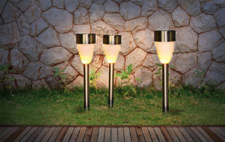 Trois bornes lumineuses plantées dans la pelouse devant un mur en pierres
