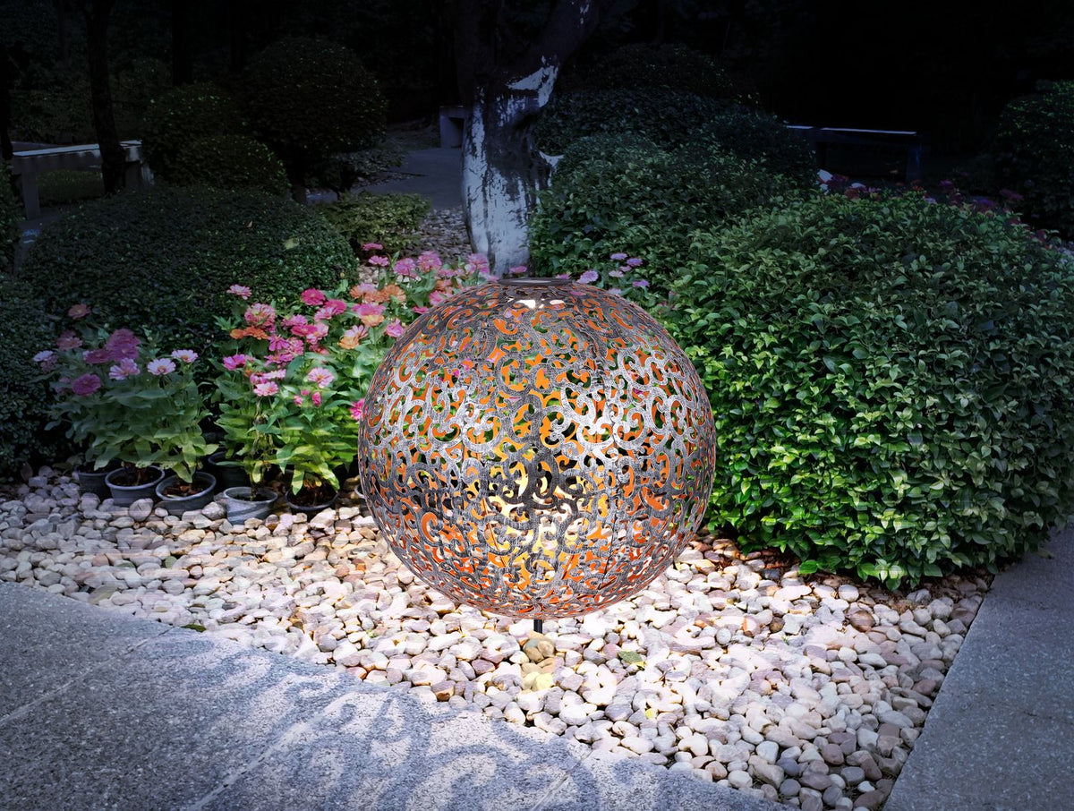 Mise en ambiance nocturne : boule solaire argentée éclairée dans un jardin fleuri.