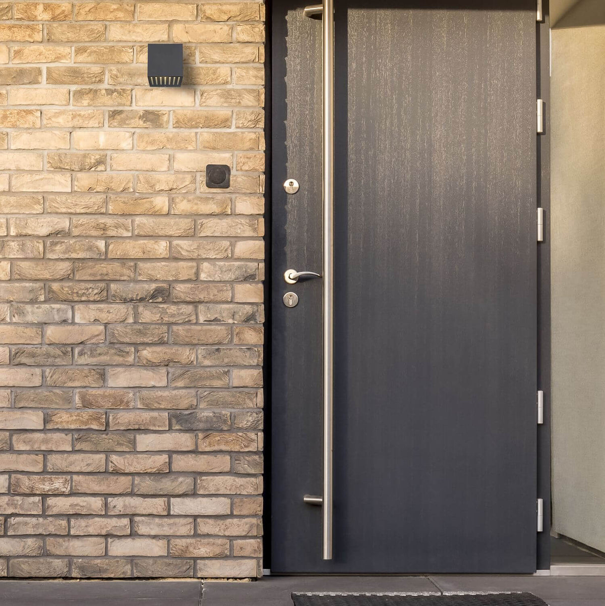 Luminaire anthracite fixé sur mur de briques, éclairant l'entrée de la maison