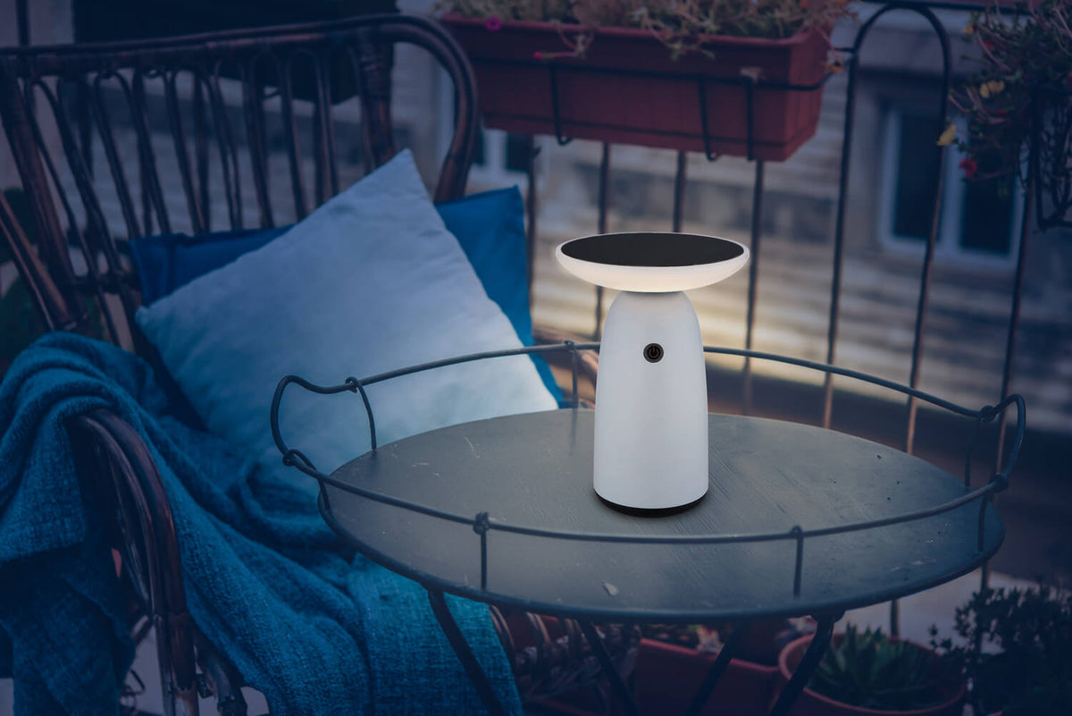 Mise en ambiance sur une table de balcon, lampe allumée près de coussins bleus