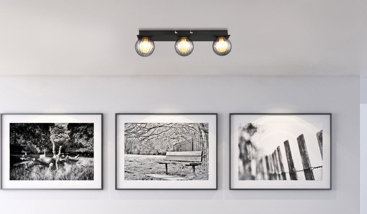 Mise en ambiance du plafonnier fixé au plafond au-dessus de trois cadres noir et blanc.