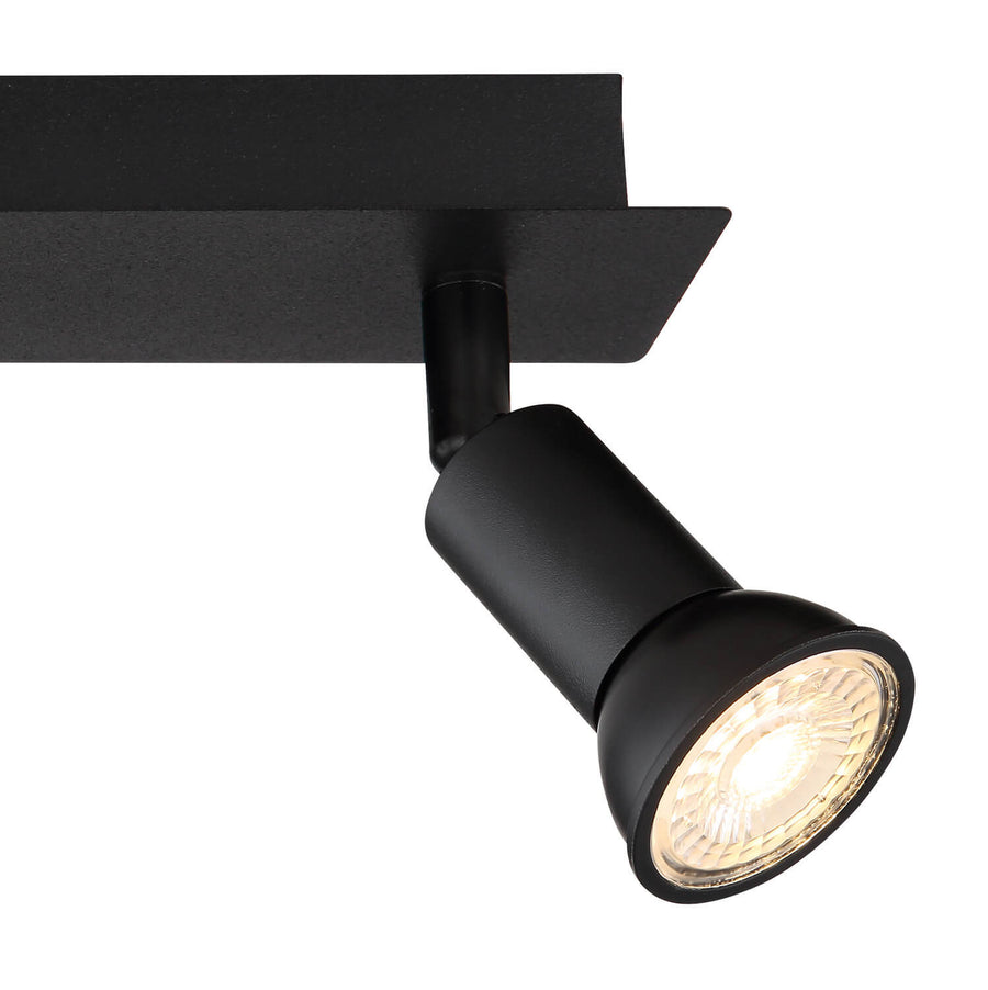 Détail rapproché d'une tête de spot noire et de son ampoule LED allumée.
