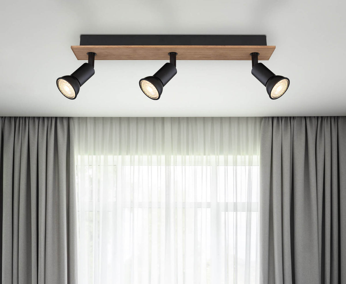 Mise en situation du spot plafond au-dessus d'une fenêtre avec rideaux gris et voilages blancs.