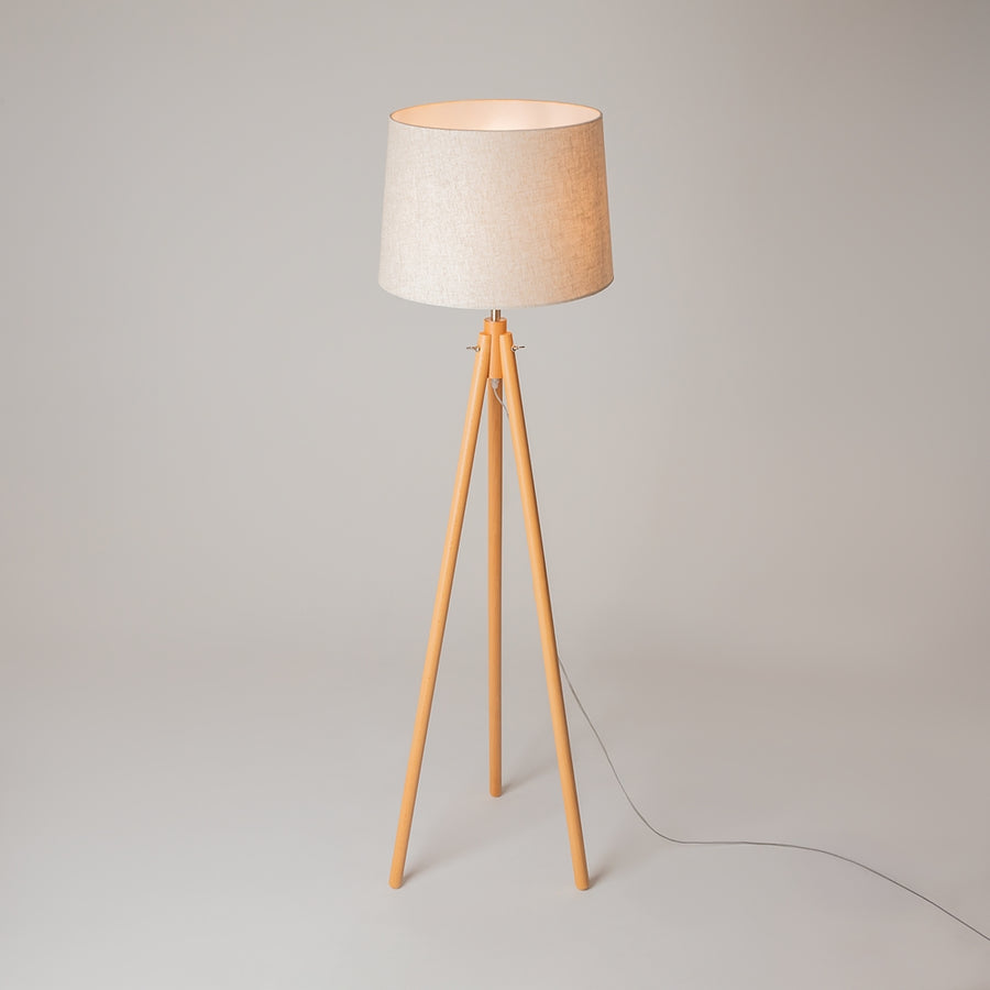 Lampadaire sur pied en bois clair, abat-jour beige et câble électrique au sol.