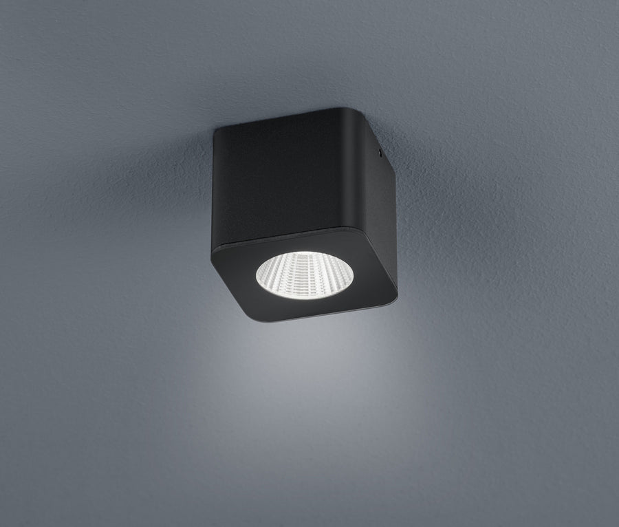 Vue rapprochée du plafonnier noir carré fixé au plafond, lentille LED ronde allumée.