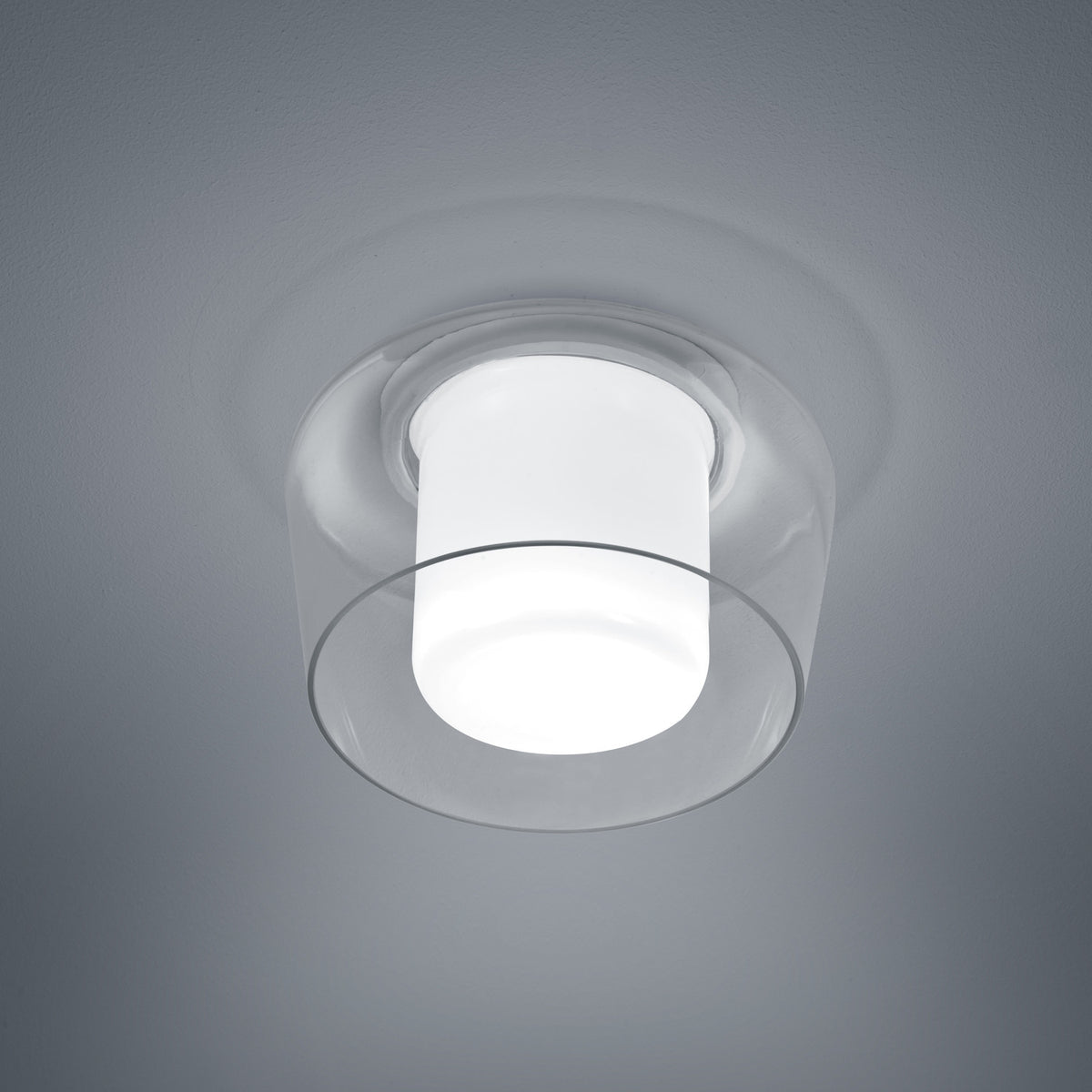 Vue rapprochée du plafonnier blanc allumé, verre transparent et diffuseur cylindrique central.