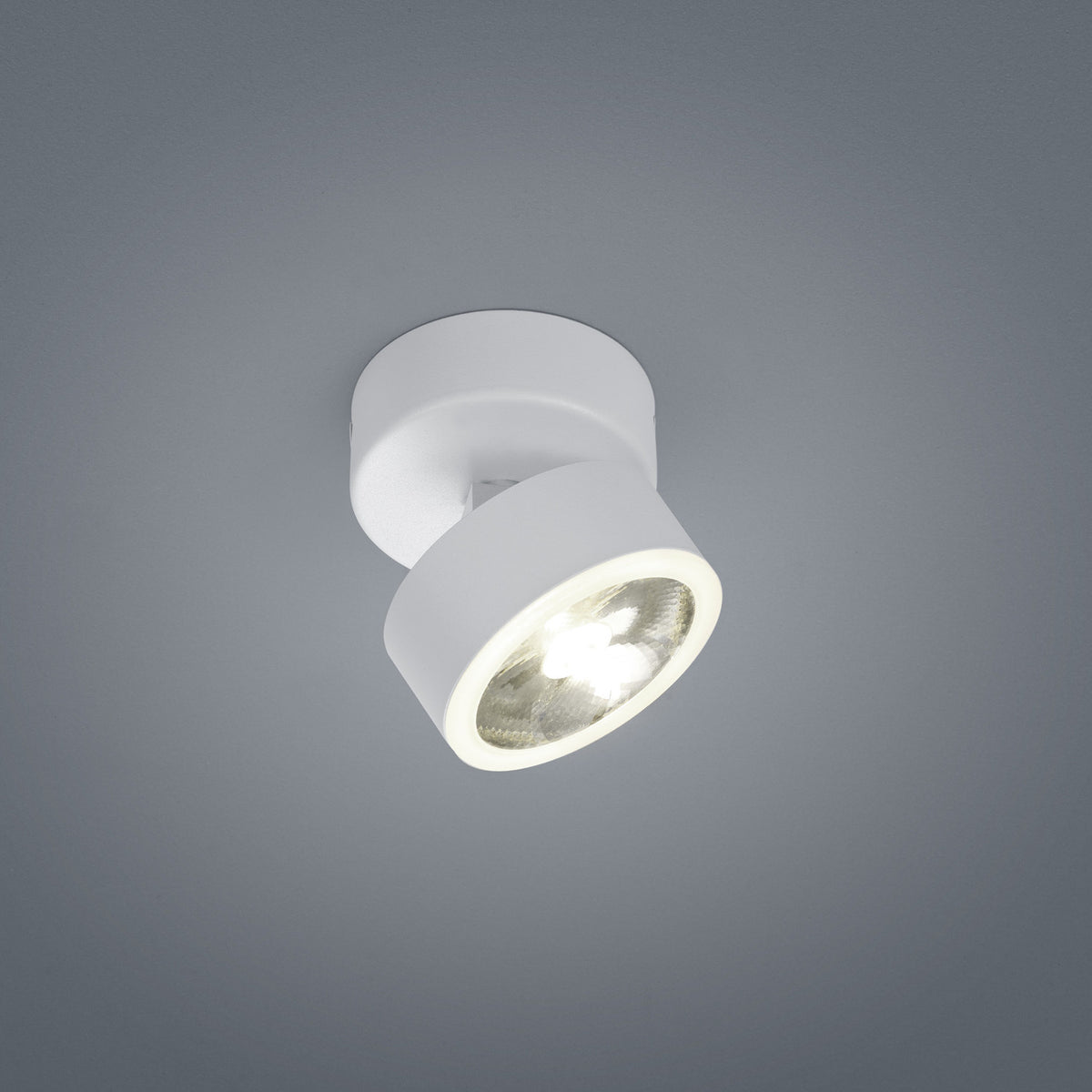 Plafonnier blanc orientable vu de face, projecteur cylindrique allumé sur fond gris