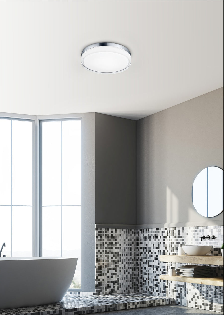 Plafonnier rond installé au plafond d'une salle de bain claire avec baignoire et vasque.