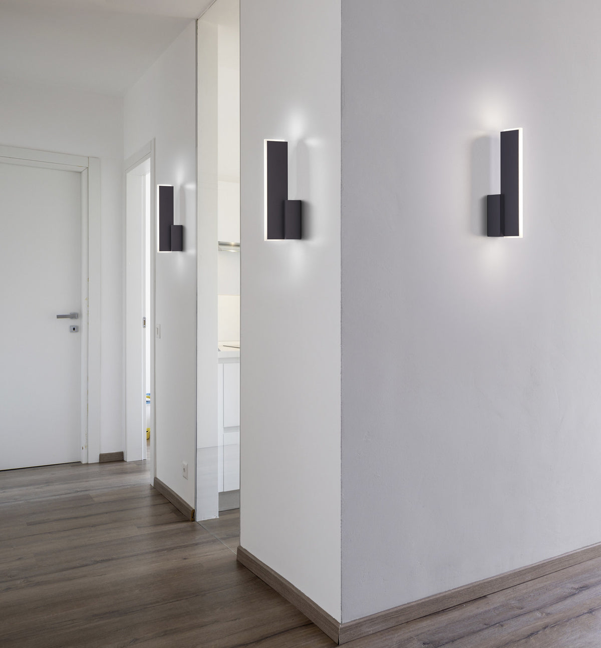 Mise en ambiance dans un couloir blanc avec trois appliques allumées éclairant les murs