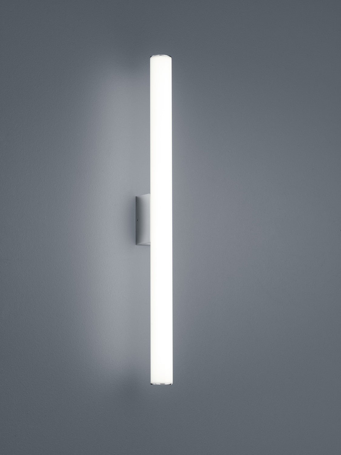 Applique murale verticale en tube lumineux blanc, fixée sur un mur gris, vue de face.