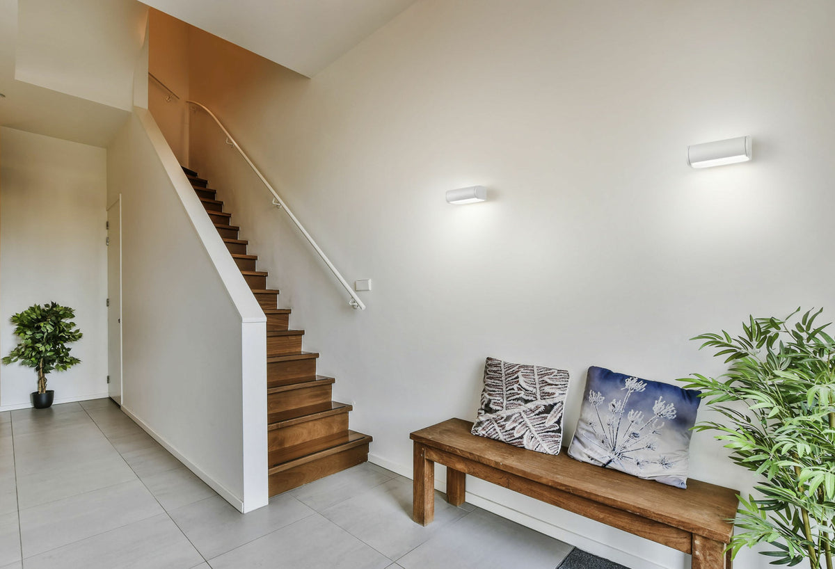 Mise en ambiance dans un hall d'entrée avec escalier en bois et deux appliques murales blanches