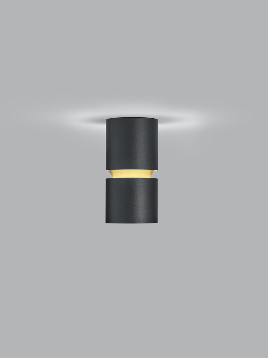 Vue de face du plafonnier cylindrique noir fixé au plafond, halo lumineux diffus