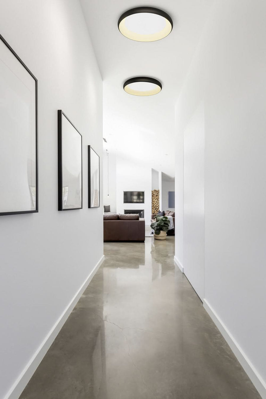 Couloir contemporain, plafonniers noirs ronds au plafond, sol béton ciré et cadres muraux