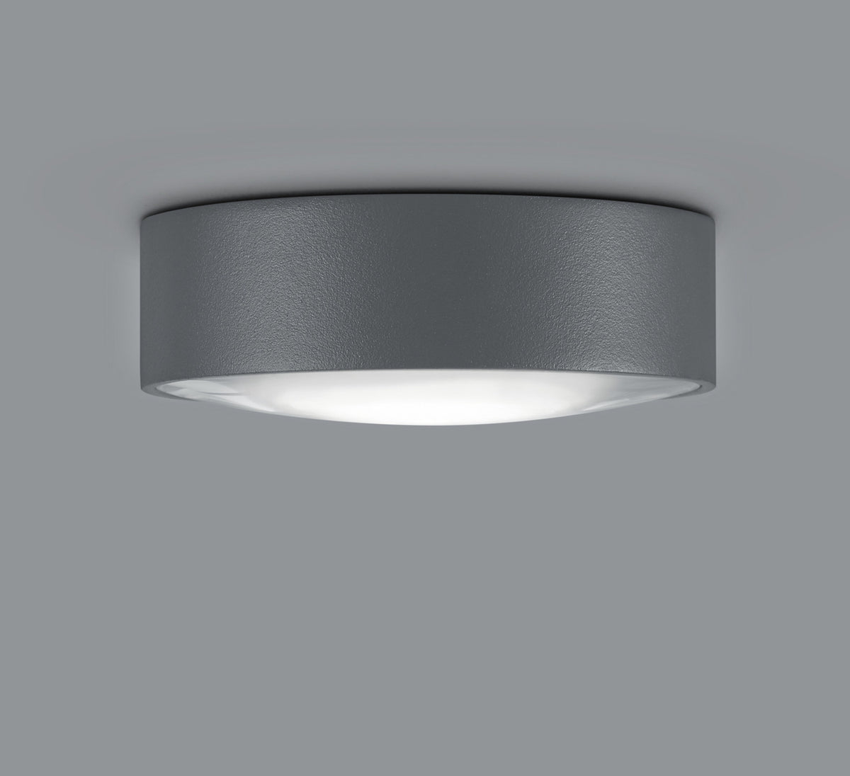 Plafonnier rond anthracite texturé vu de biais, diffuseur blanc allumé sous la coupelle