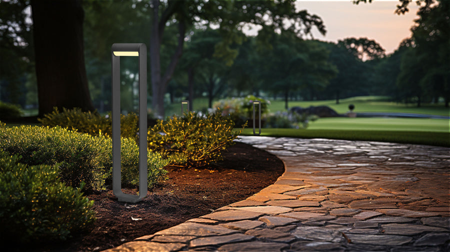 Borne lumineuse verticale anthracite éclairant une allée de jardin pavée au crépuscule