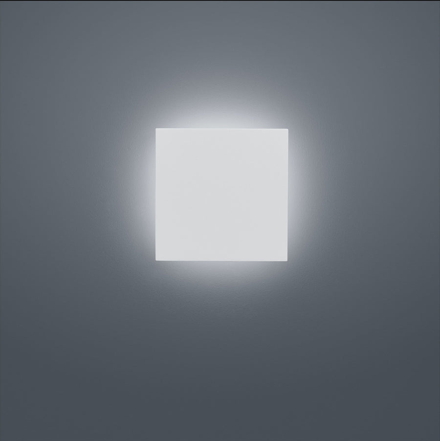 Face avant du luminaire carré blanc allumé, halo lumineux diffus sur mur gris