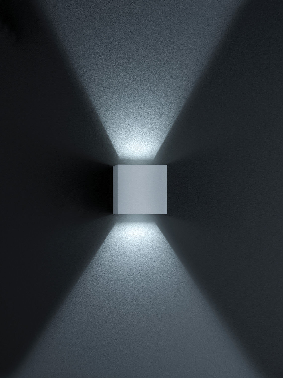 Applique cubique grise sur mur sombre projetant deux cônes lumineux verticaux
