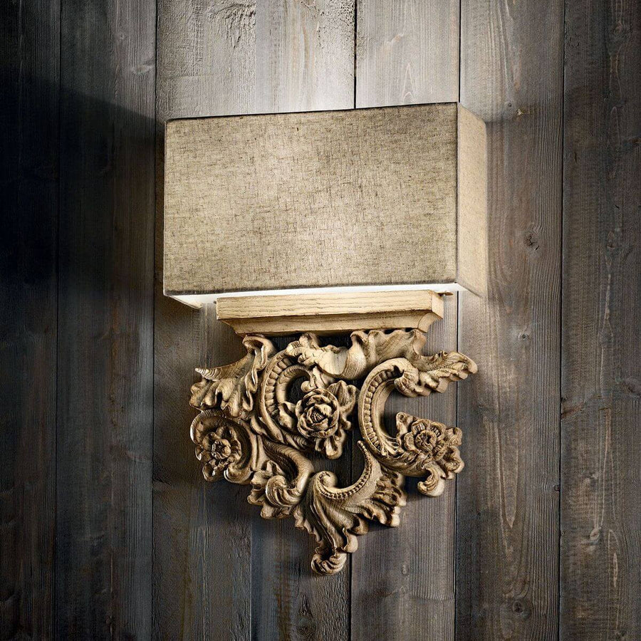 Applique murale allumée fixée sur un mur en lambris sombre, abat-jour beige et base sculptée.