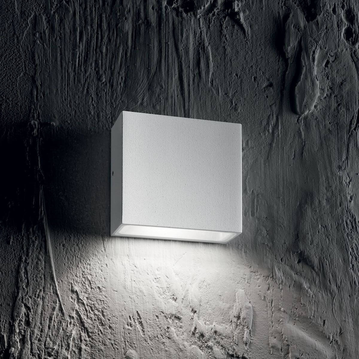 Mise en ambiance de l'applique blanche éclairant un mur sombre très texturé