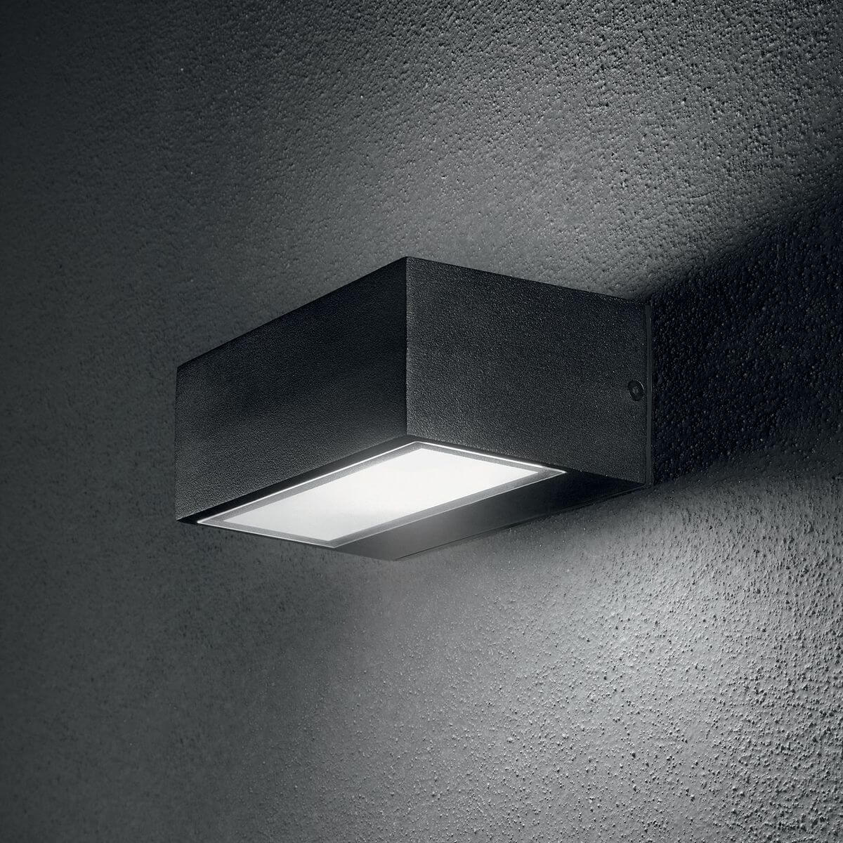 Mise en ambiance de l'applique noire allumée sur un mur texturé gris foncé