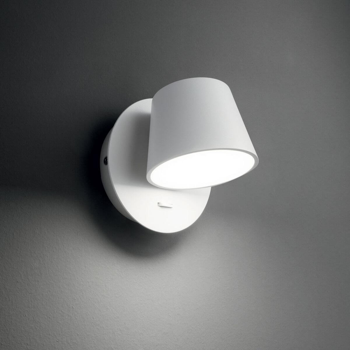 Mise en ambiance sur mur gris, applique blanche allumée diffusant une lumière douce