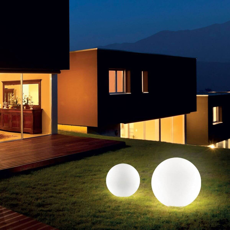 Deux lampadaires sphériques blancs allumés sur une pelouse devant une maison au crépuscule