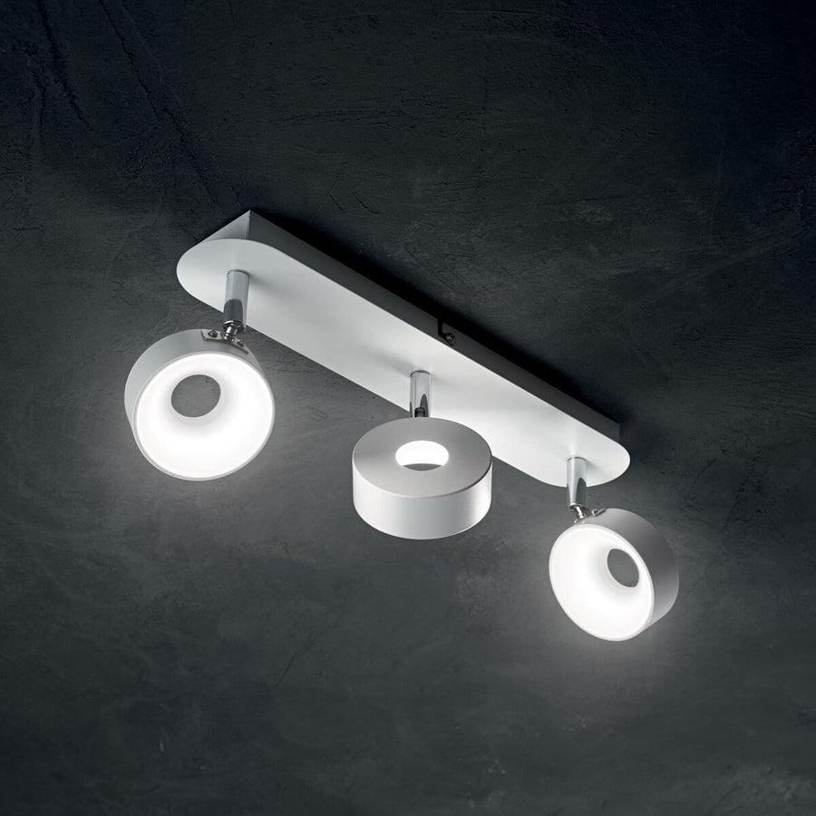 Plafonnier blanc allumé fixé au plafond sombre, trois spots ronds lumineux