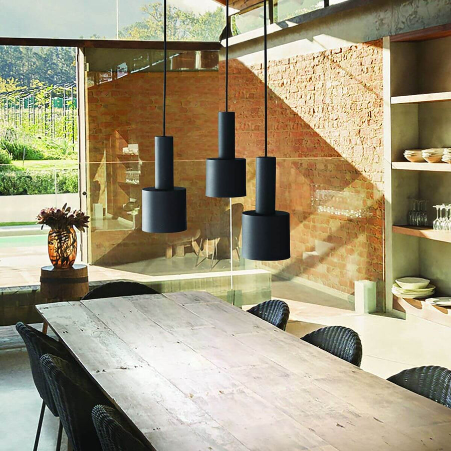 Trois suspensions noires suspendues au-dessus d'une table en bois dans un intérieur.
