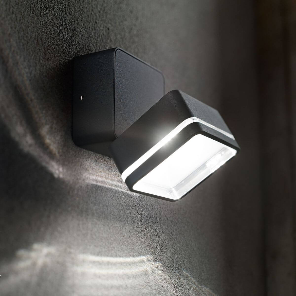 Applique murale allumée sur mur sombre, halo lumineux et ombre portée