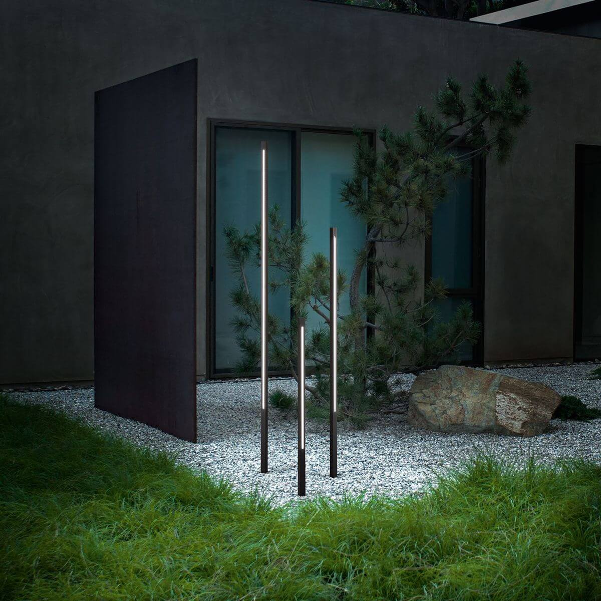 Trois lampadaires verticaux allumés dans un jardin de gravier avec pin