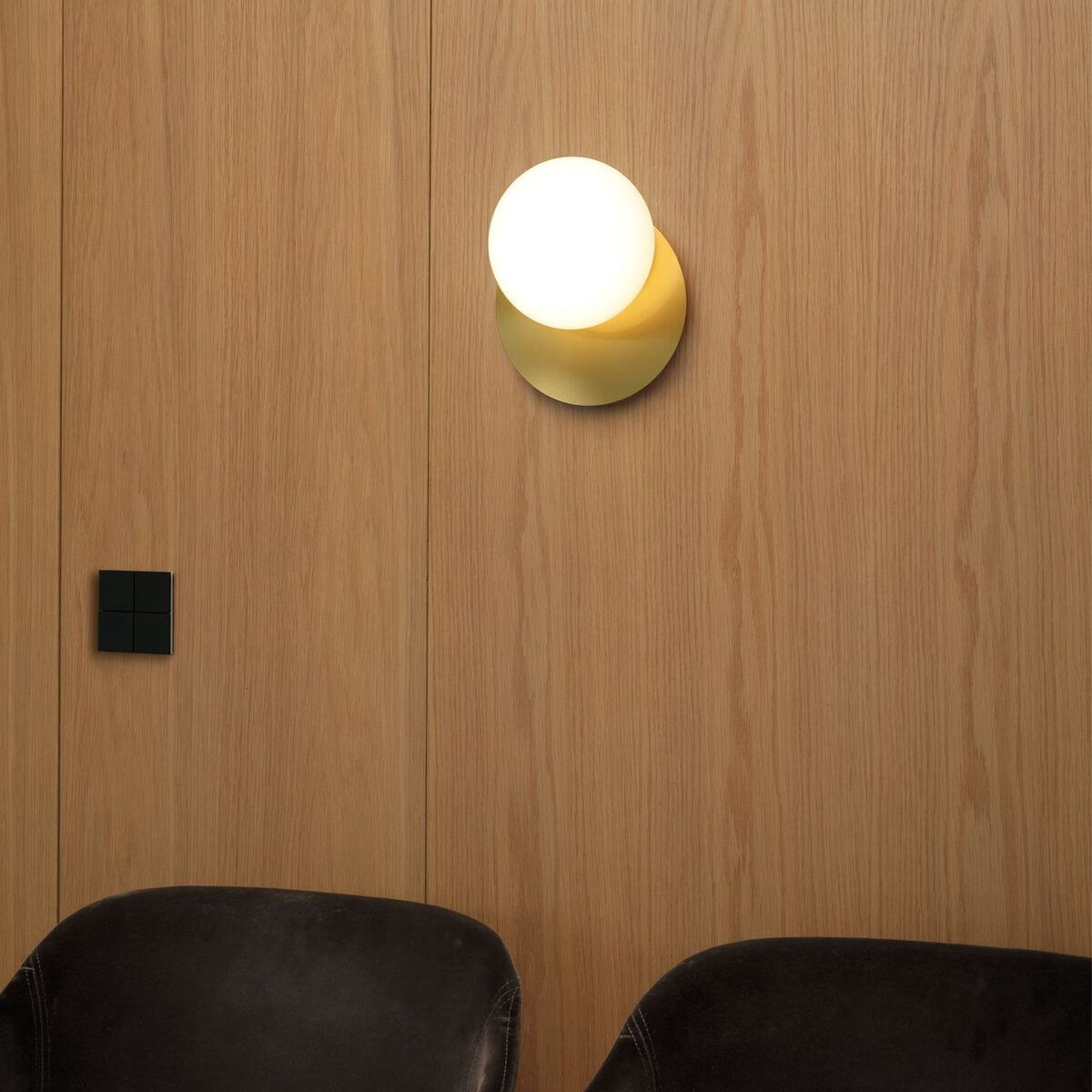 Applique murale fixée sur paroi en bois clair, ambiance intérieure avec assises en cuir.