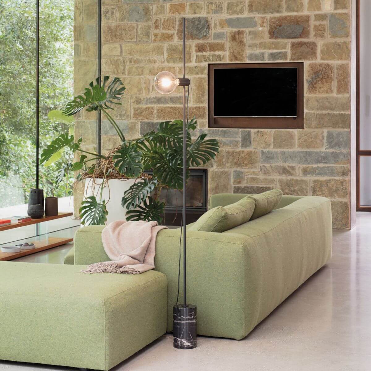 Mise en ambiance d'un salon avec lampadaire allumé, canapé vert et mur en pierre