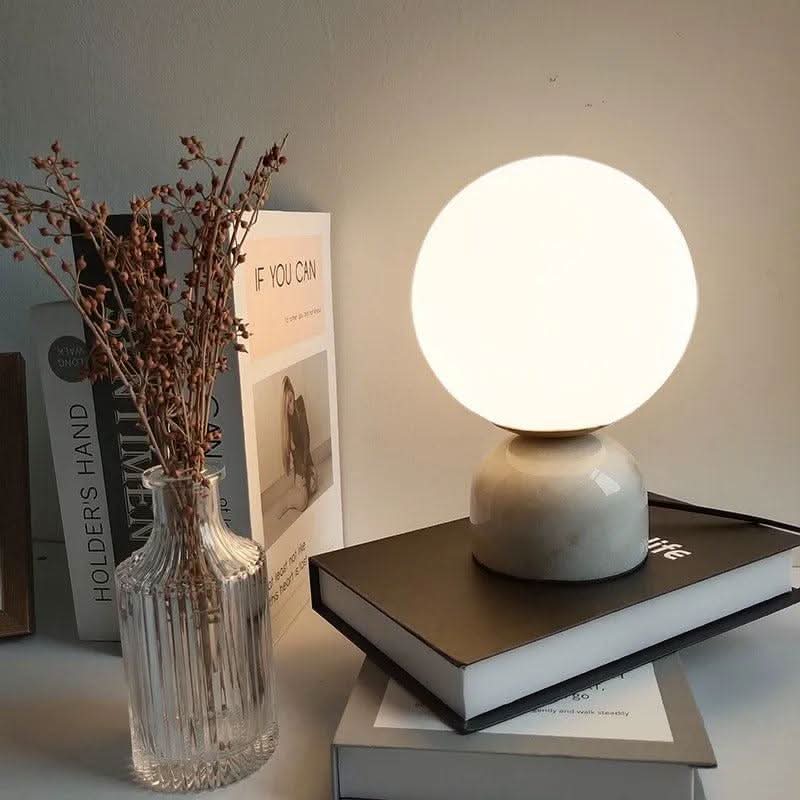 Lampe boule grise posée sur des livres, vase de fleurs séchées à gauche
