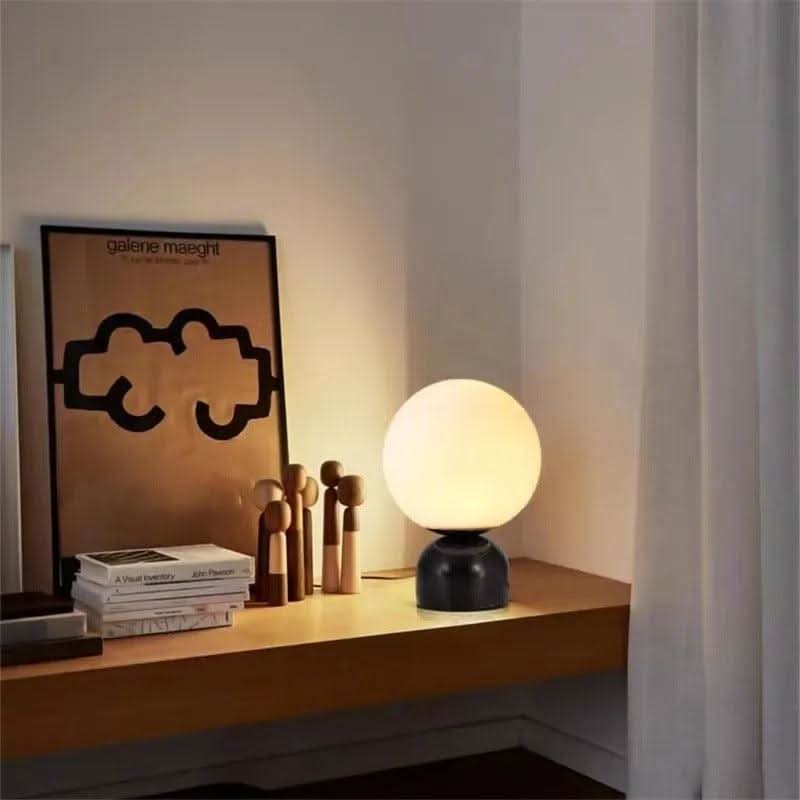 Petite lampe à base noire sur bureau en bois, affiche encadrée derrière