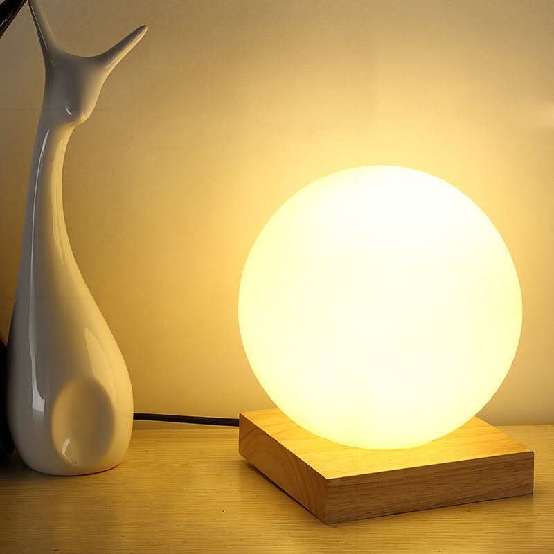 Boule lumineuse sur base carrée en bois, près d'une sculpture blanche en forme de girafe.