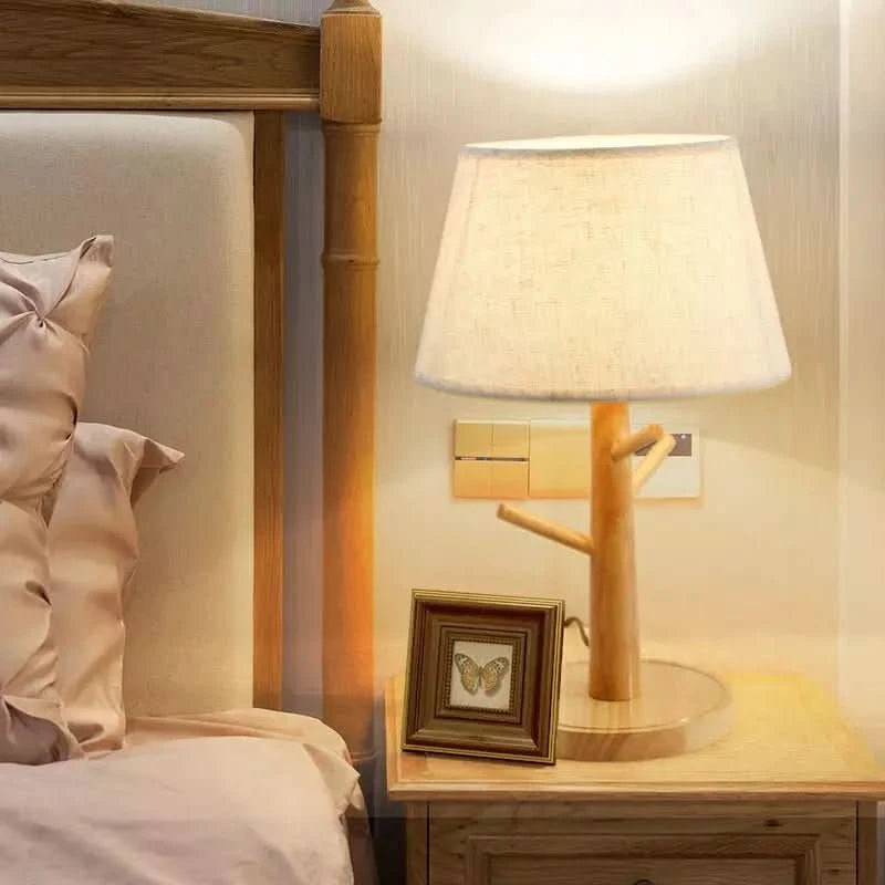 Lampe posée sur une table de chevet près d'un lit, allumée, avec cadre photo