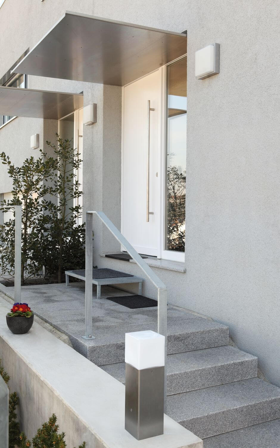 Vue de l'allée et des marches, applique inox fixée près de la porte blanche