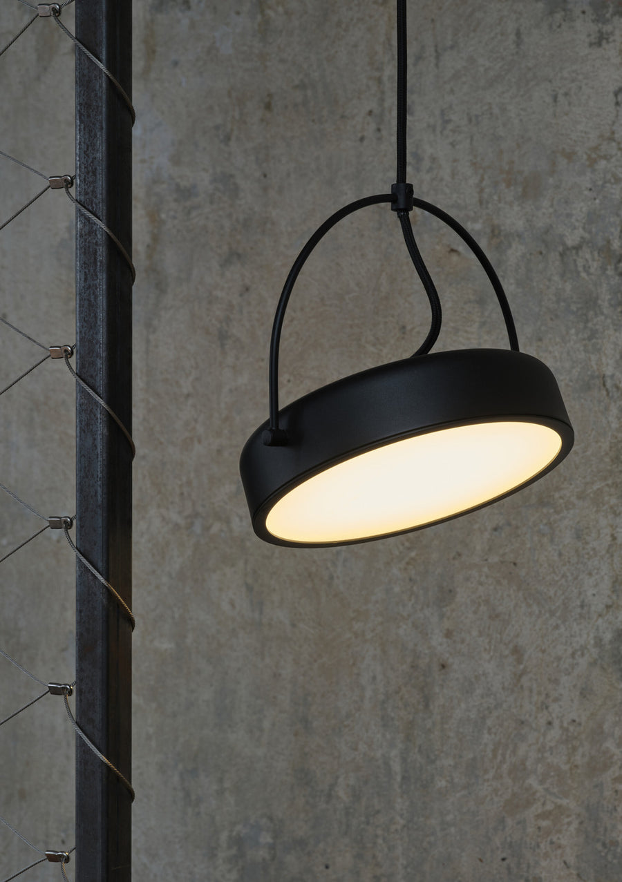 Détail de la lampe allumée diffusant une lumière chaude sur un mur béton.