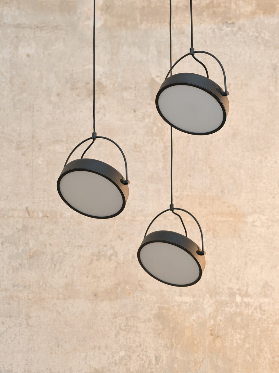 Détail rapproché des trois disques noirs suspendus devant un mur beige clair.
