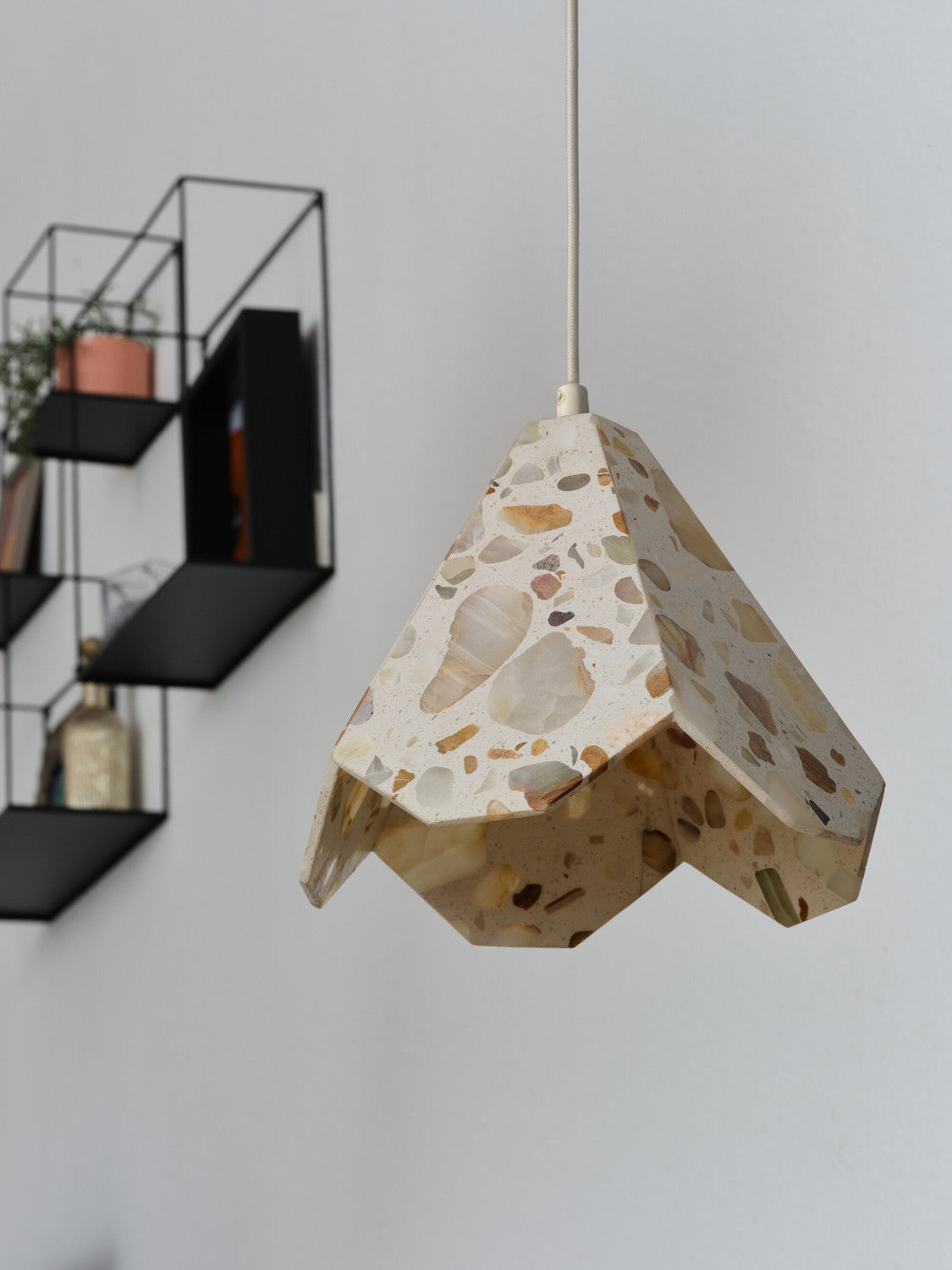 Gros plan sur l’abat-jour facetté en terrazzo beige, étagères noires en arrière-plan.