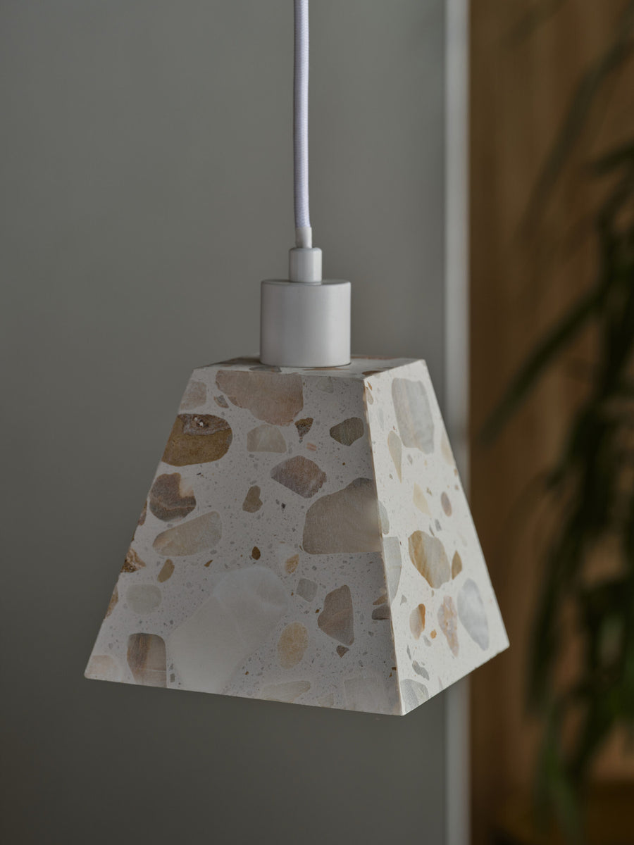Gros plan sur l'abat-jour carré en terrazzo beige et blanc, suspendu près d'une plante.
